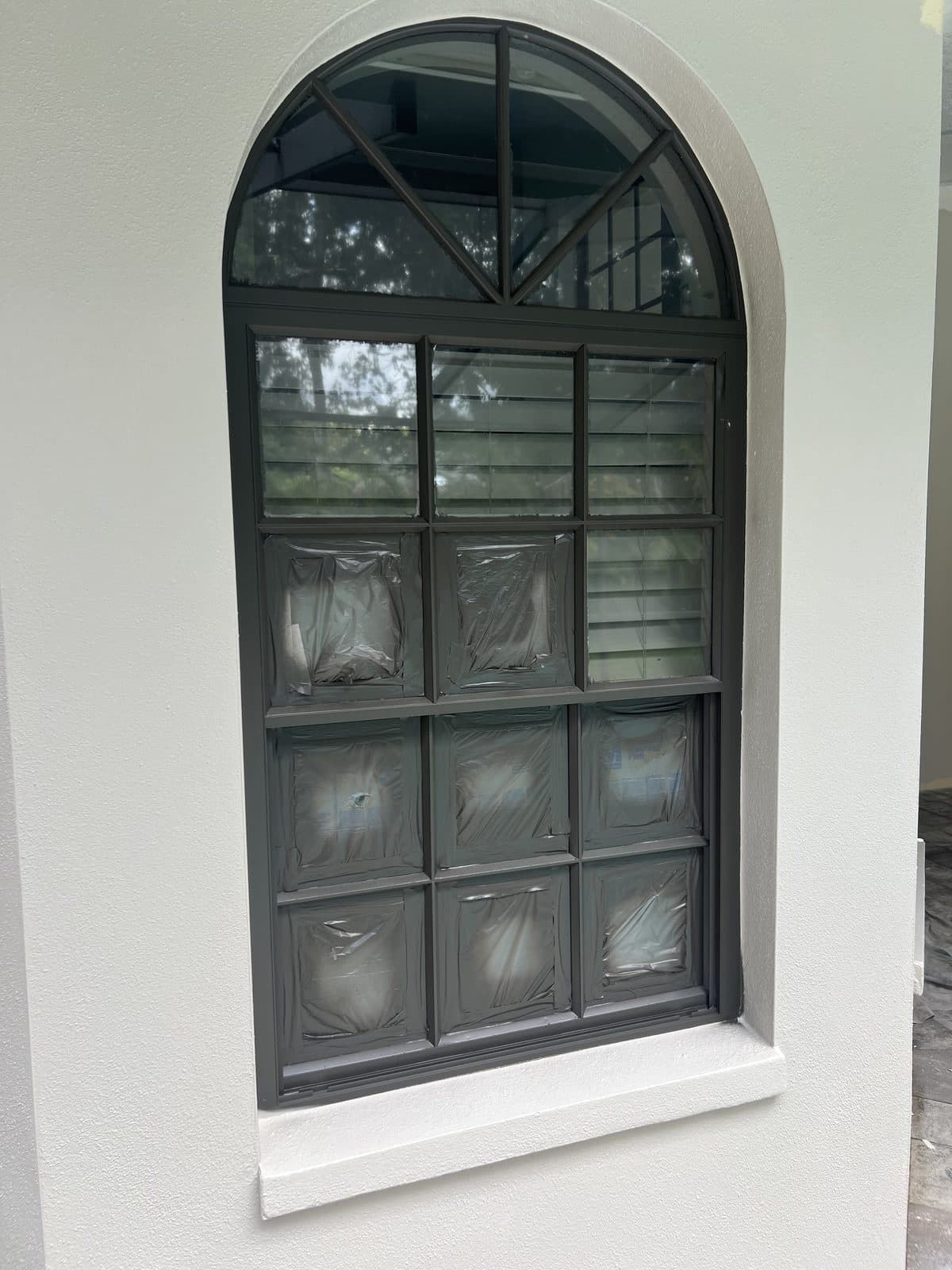 Arched window masked off during exterior prep, with fresh paint on the stucco around it